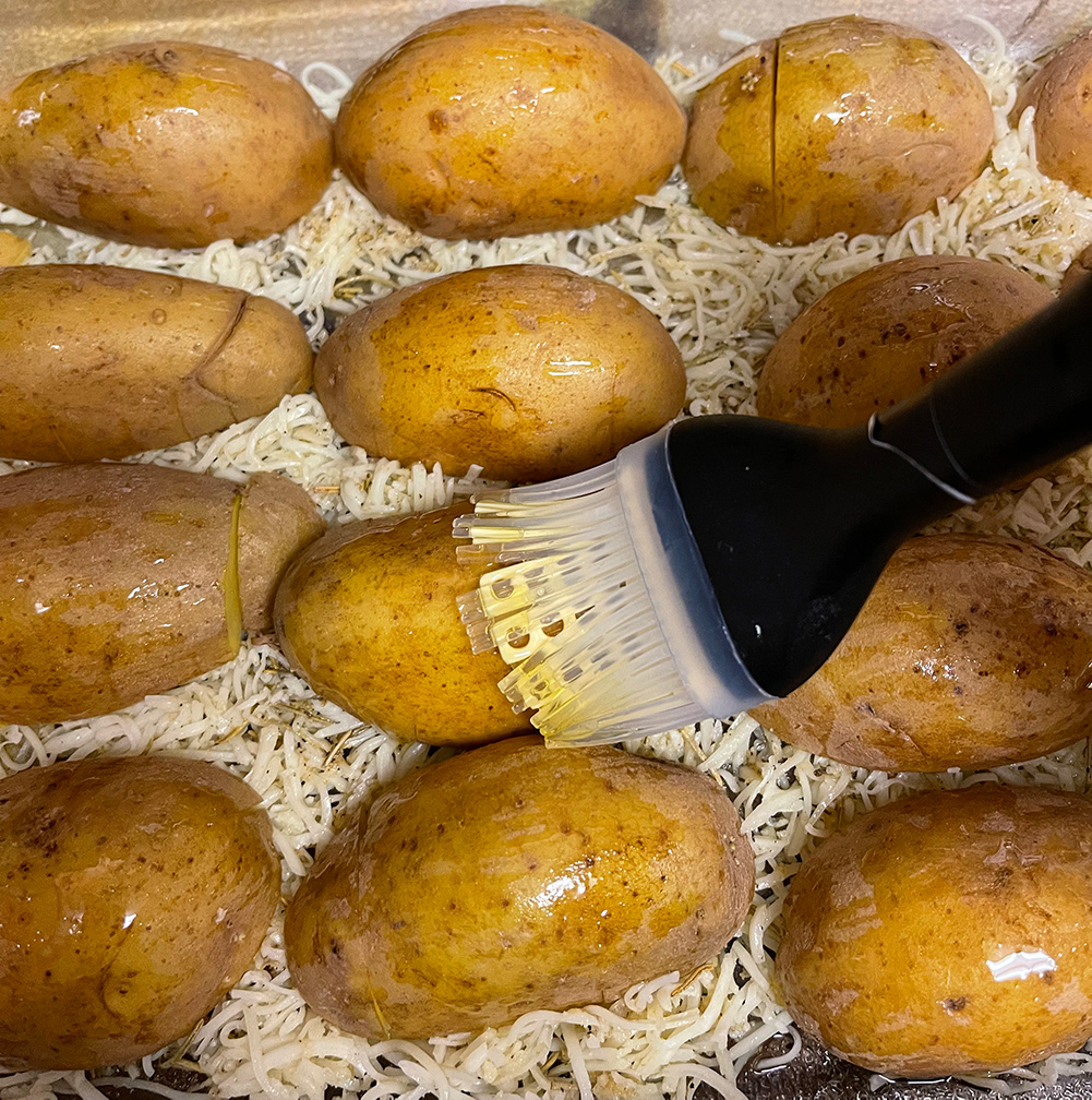 Photo of potatoes arranged in a baking dish on top of a layer of shredded cheese, being brushed with olive oil