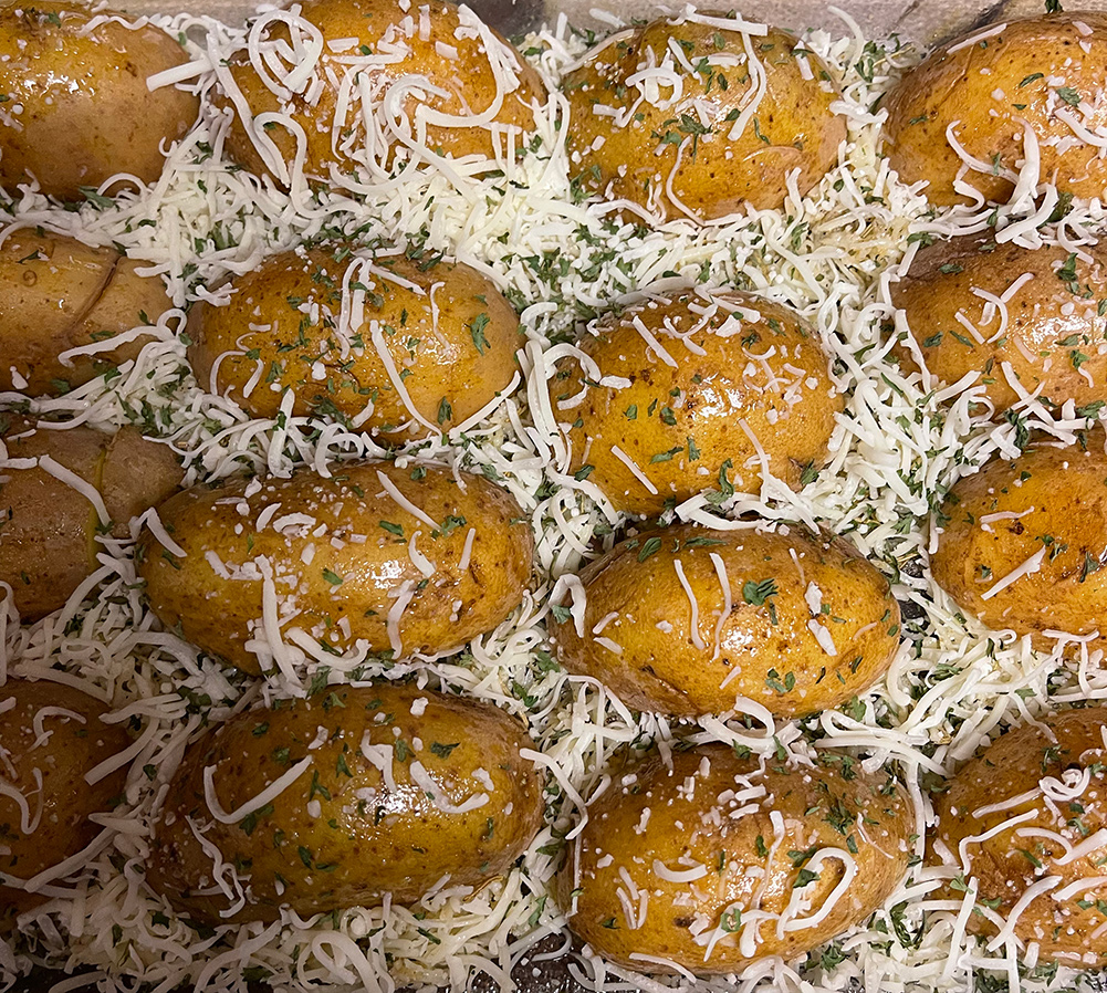 Photo of potato halves facedown in a baking dish, with cheese and dried parsley sprinkled on top